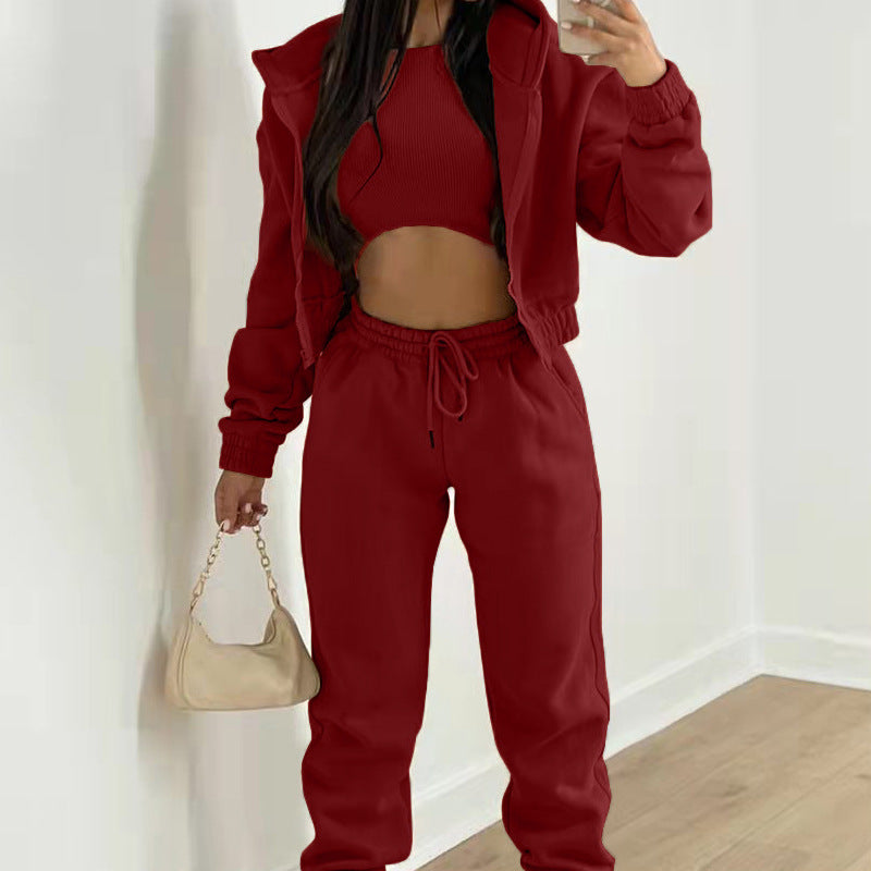 Deep red three-piece lounge set: ribbed crop top, fleece-lined hoodie, and drawstring joggers. Includes a beige bag.