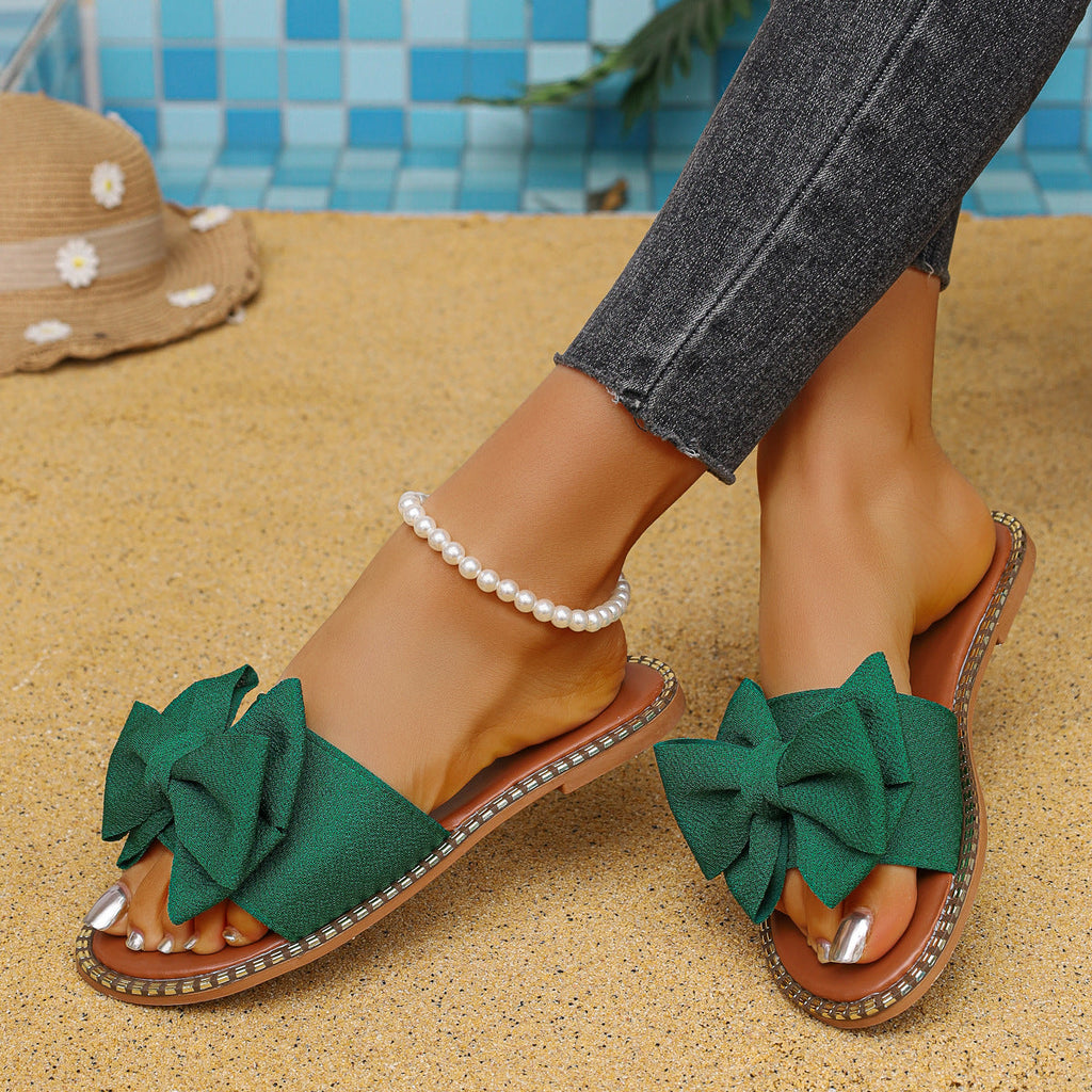 Plush Fashion Hub bowknot embellished flat sandals with open toe design and stylish straps on a white background.