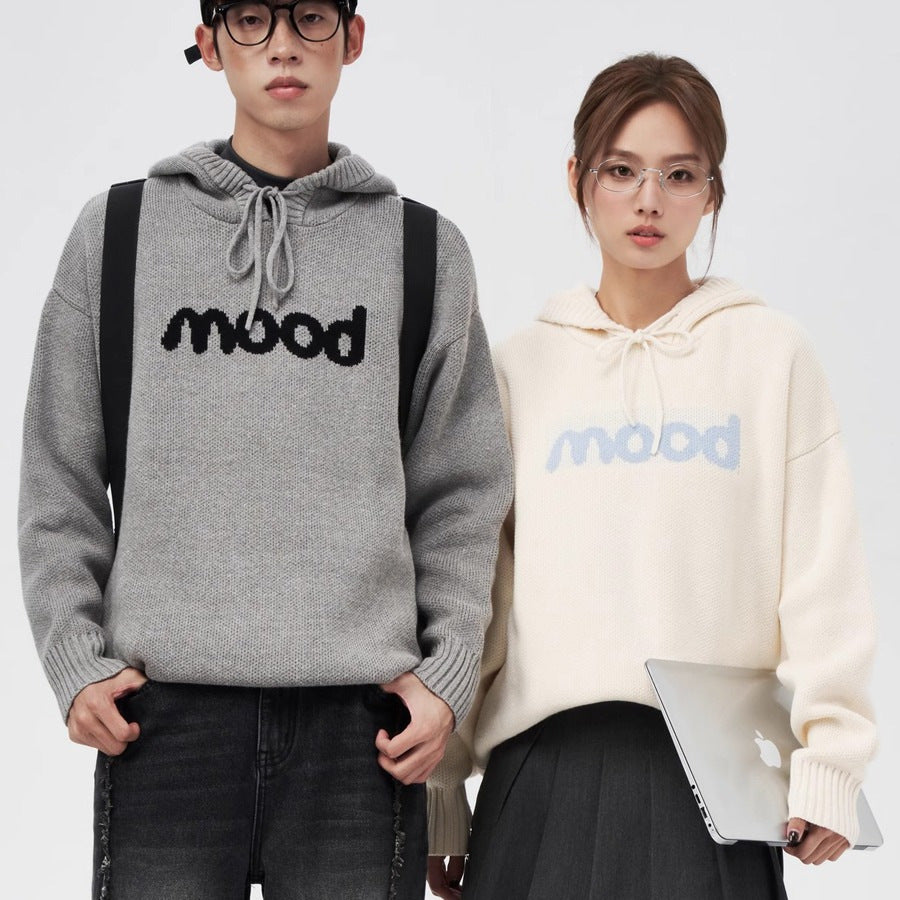 Two people wearing knit hoodies with "mood" text: one grey with black text, one off-white with blue text.