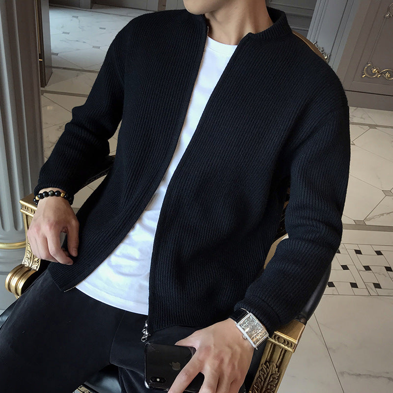 A man wears a black knitted zip-up cardigan over a white t-shirt, featuring a ribbed pattern and stand collar.