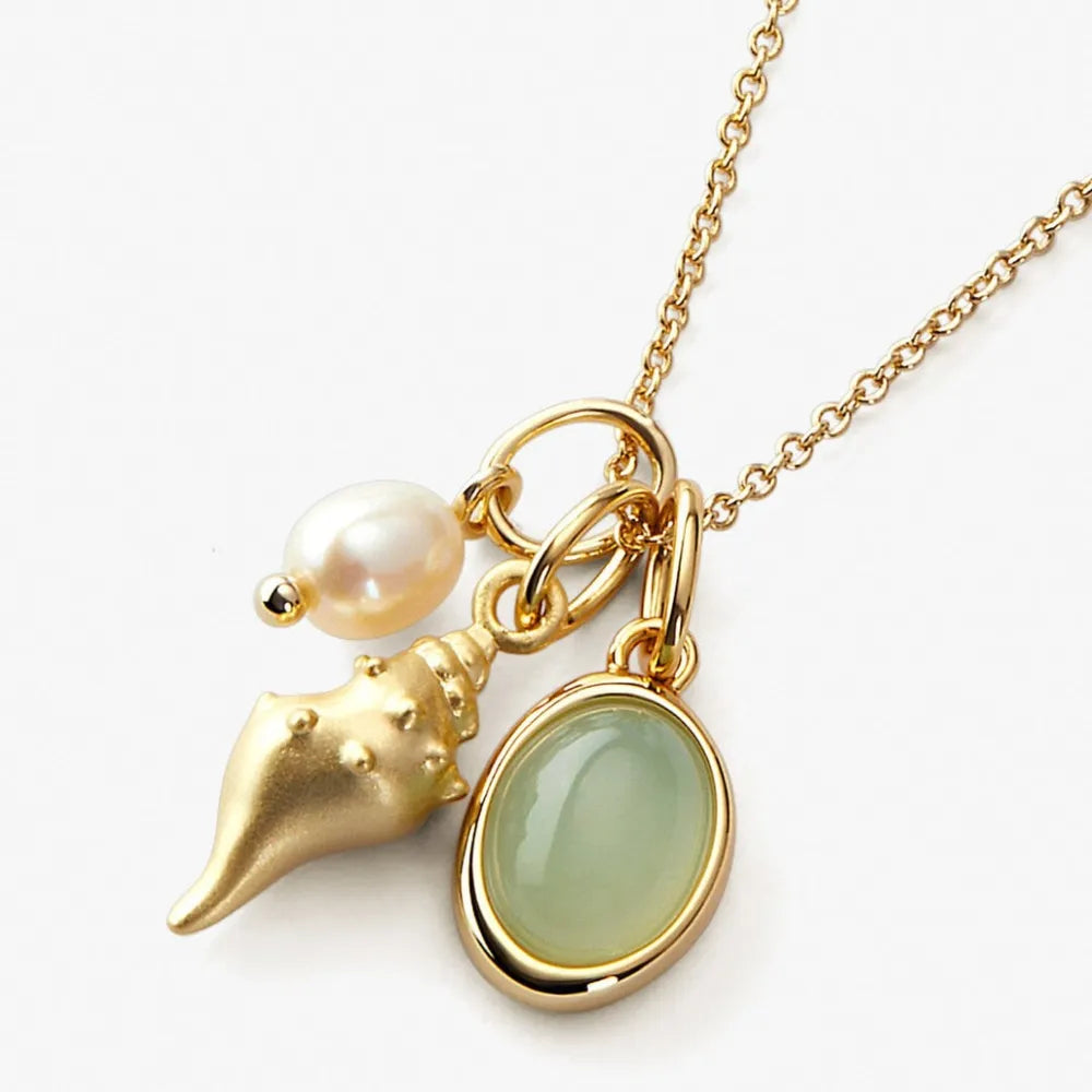 Gold chain necklace with a pearl, gold seashell charm, and an oval light green stone pendant.