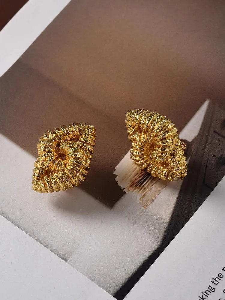 A pair of gold textured metal earrings with a spiral, knotted abstract style, displayed on magazine pages.
