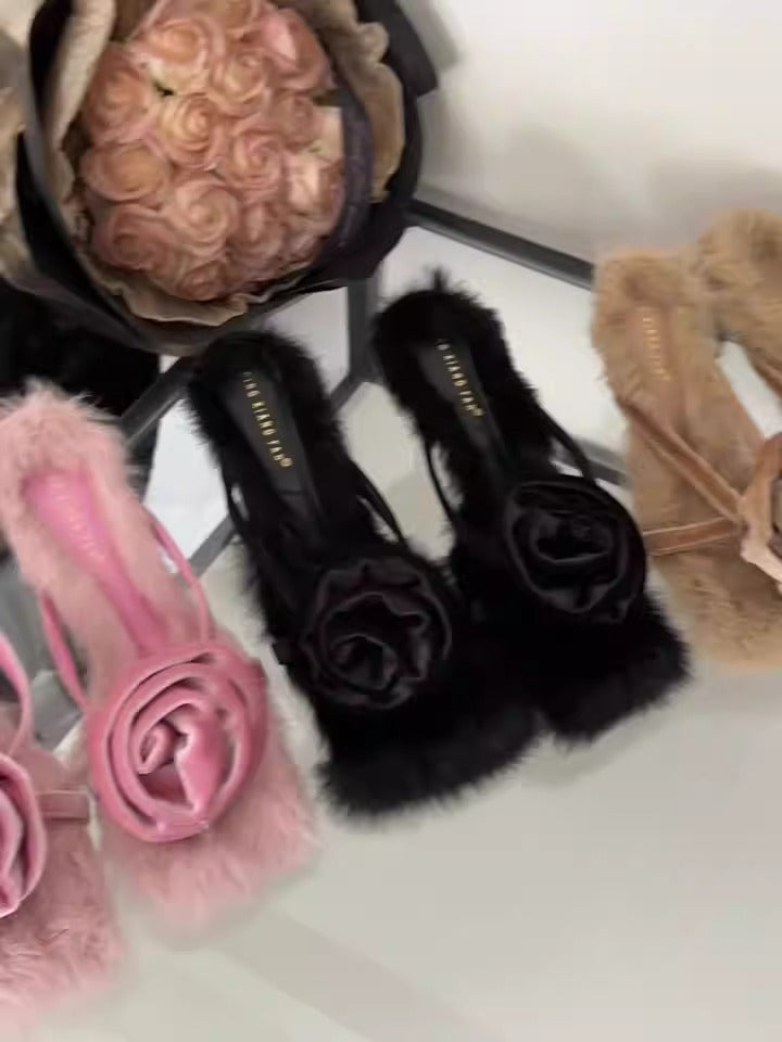 Black high-heeled sandals featuring fluffy faux fur trim and an elegant satin rose embellishment on the toe strap.