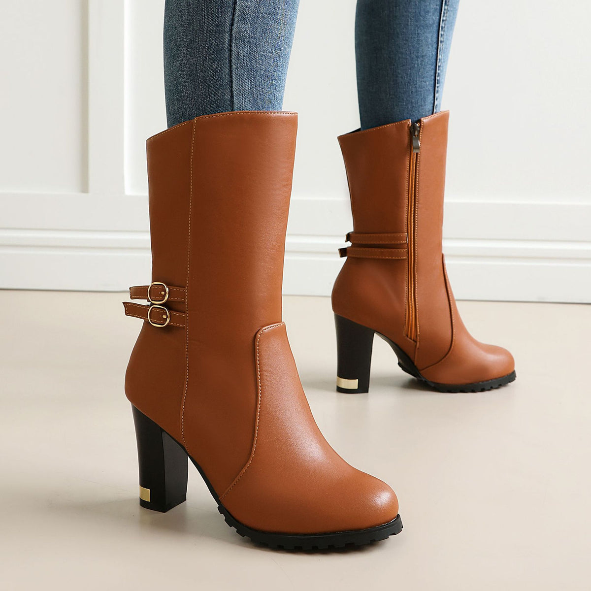 Tan mid-calf faux leather boots with chunky heels, side zippers, decorative double-buckle straps, and lug soles.