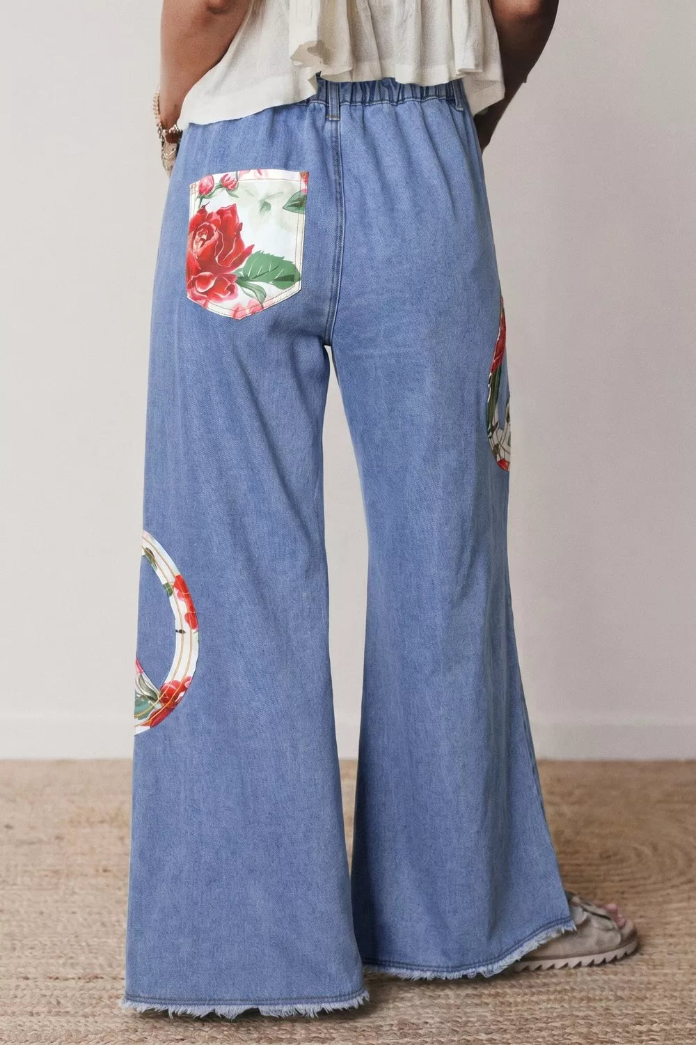 Floral peace sign wide-leg jeans by Plush Fashion Hub featuring colorful floral embroidery on light denim.