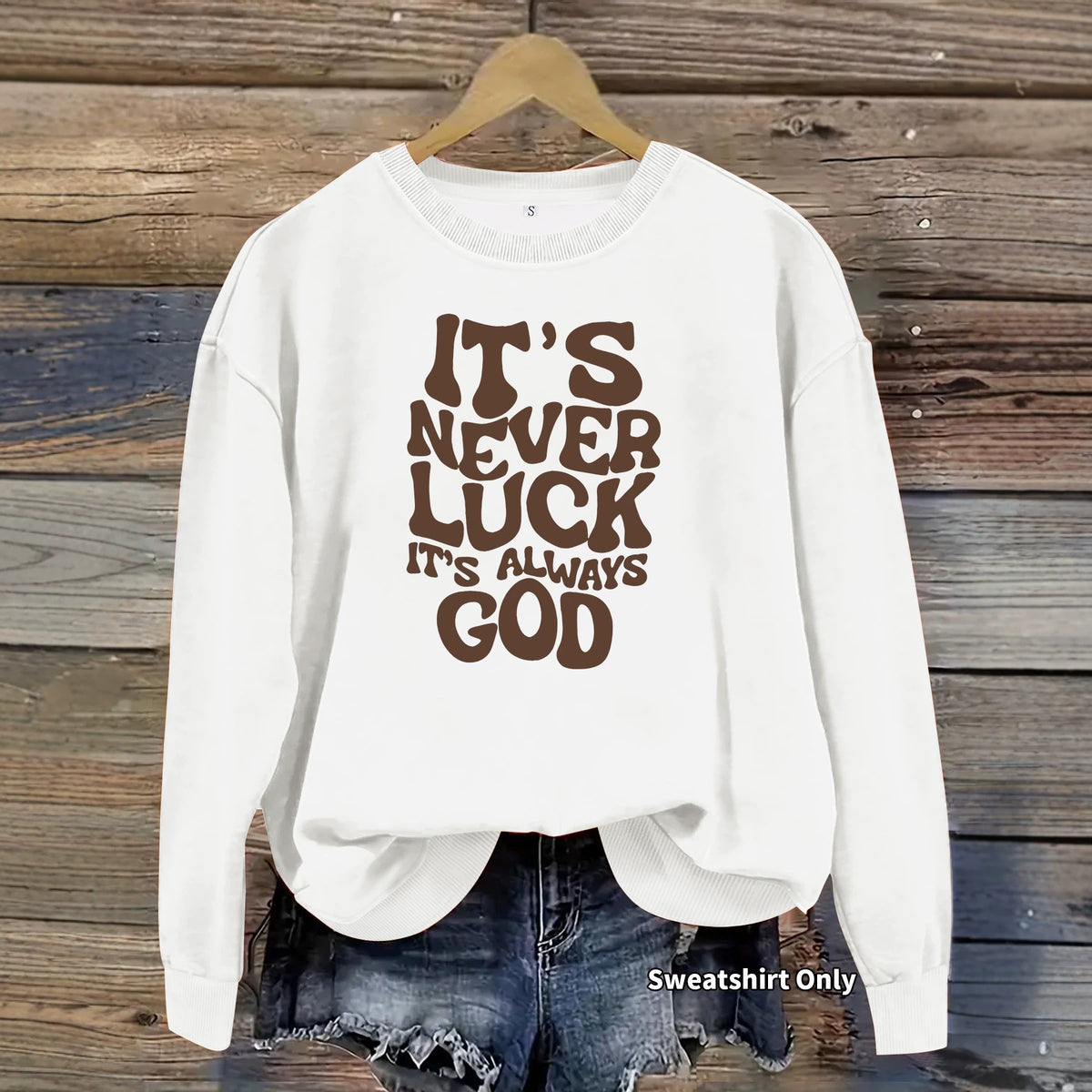 White crewneck sweatshirt with long sleeves, featuring brown retro typography reading "It's Never Luck It's Always God".