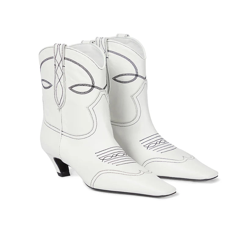 White leather cowboy boots featuring black contrast stitching, pointed toes, and low heels.
