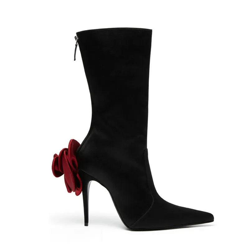Black satin mid-calf high-heeled boot, pointed toe, back zipper, with large red flower accent on heel.