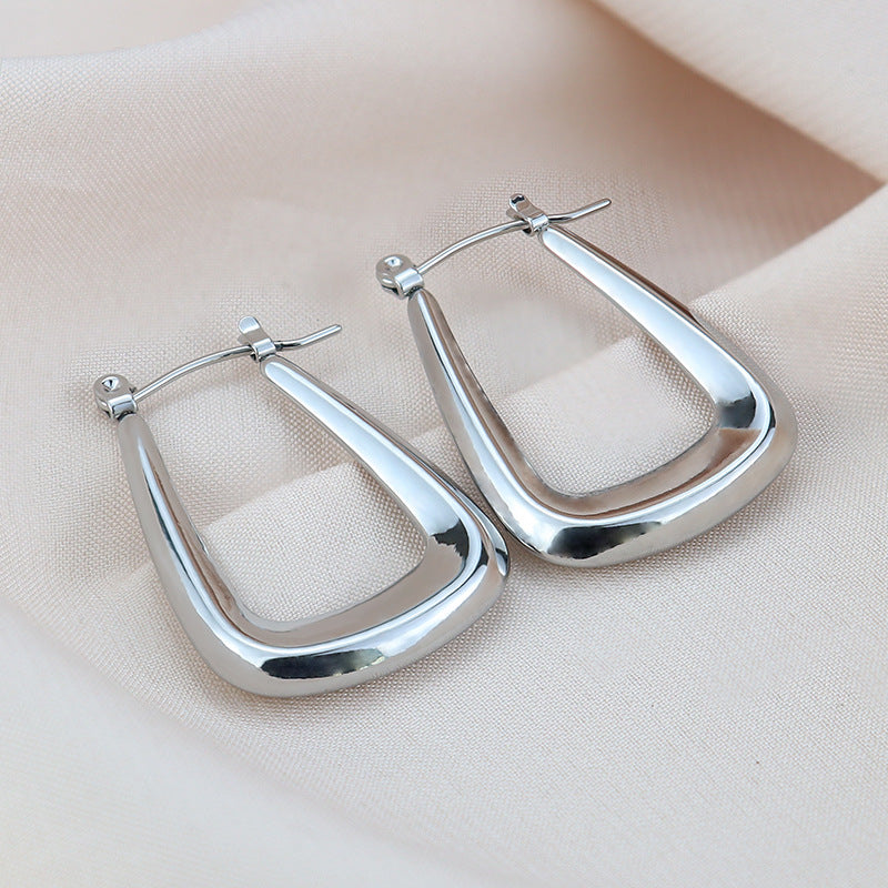 Silver rectangular hoop earrings with rounded corners and hinged closures on beige fabric.