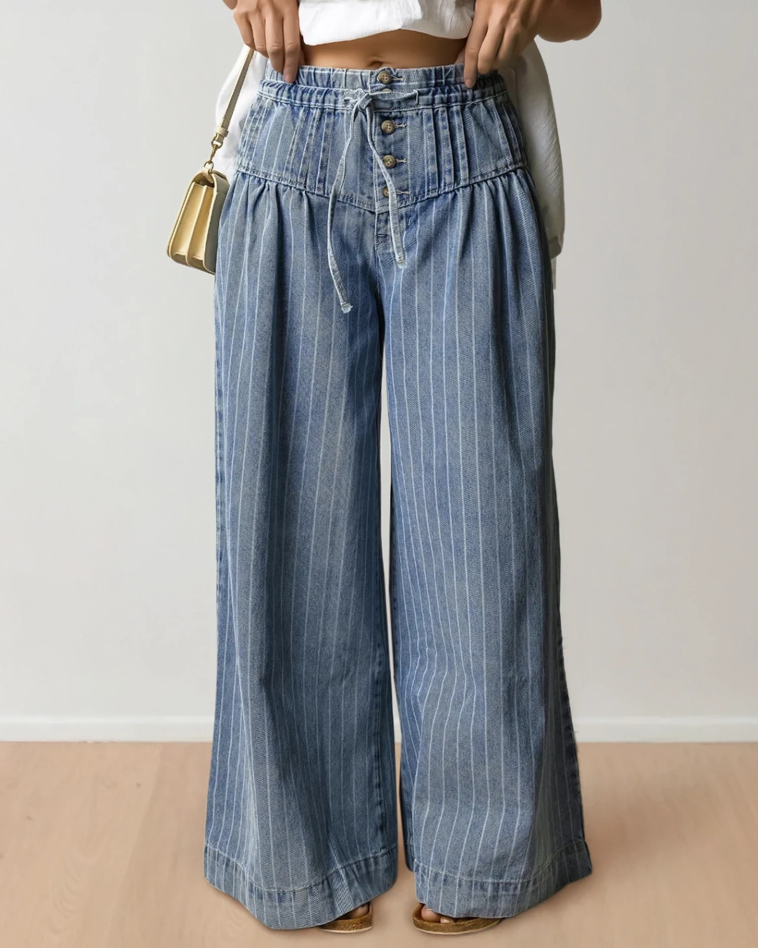 Blue striped wide-leg denim jeans feature a high-waisted pleated waistband with buttons and a drawstring.