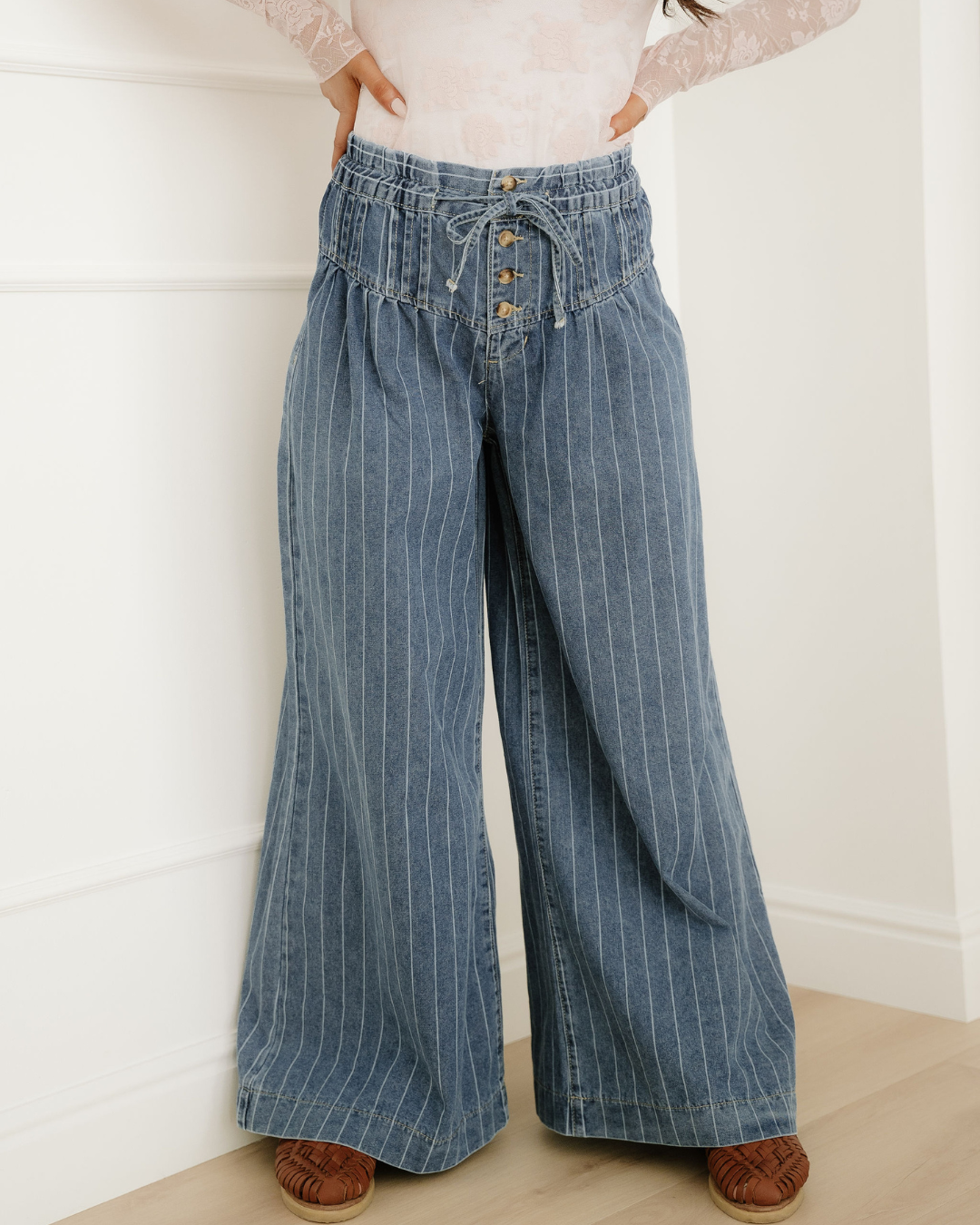 Blue pinstripe wide-leg jeans featuring a high pleated waist, drawstring, and front buttons.