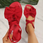 Shopimist bow embellished flat sandals featuring sleek straps and decorative bow accents on a neutral background.