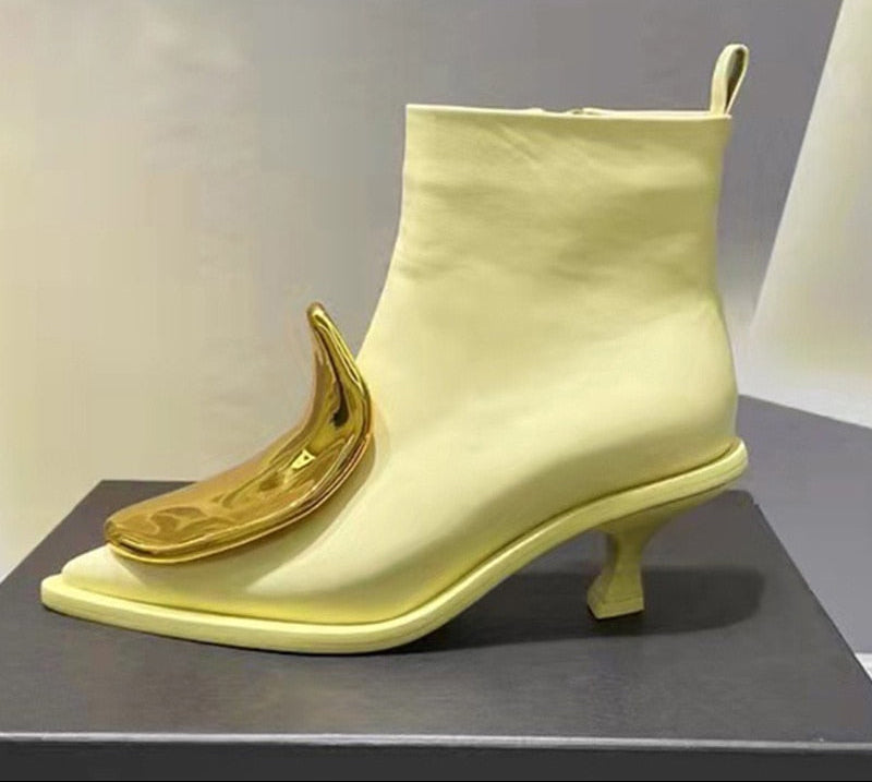 Pale yellow leather ankle boot featuring a pointed toe, kitten heel, and a shiny gold banana-shaped toe accent.