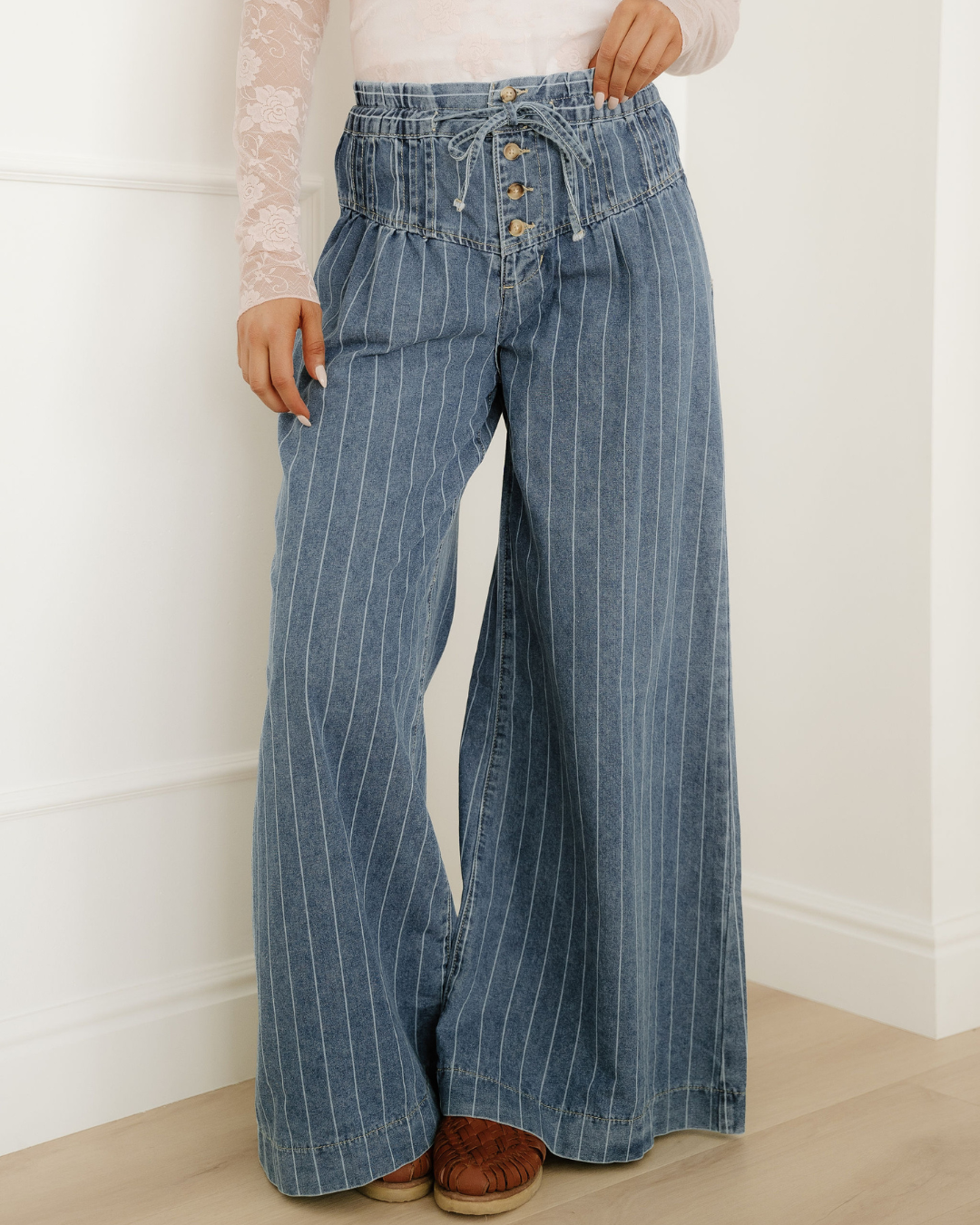 Blue pinstripe denim wide-leg jeans featuring a high pleated waist with a button placket and drawstring.