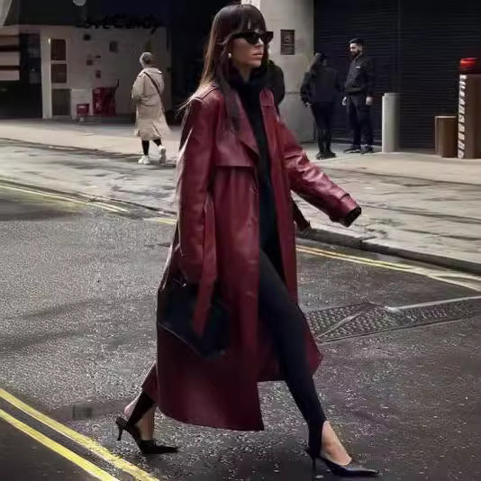 Burgundy faux leather trench coat worn open with a black top, stirrup leggings, and heels on a city street.