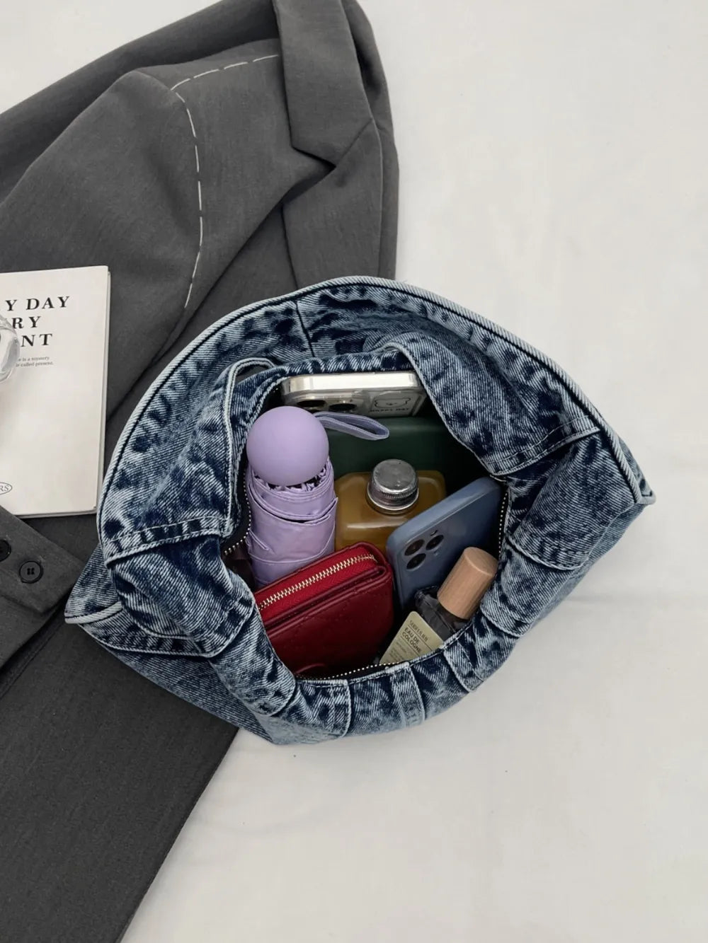 Blue denim shoulder bag, casual style, holding personal items like a purple umbrella, phone, and red wallet.