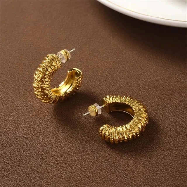Gold metal textured chunky hoop earrings with push backs on a brown surface.