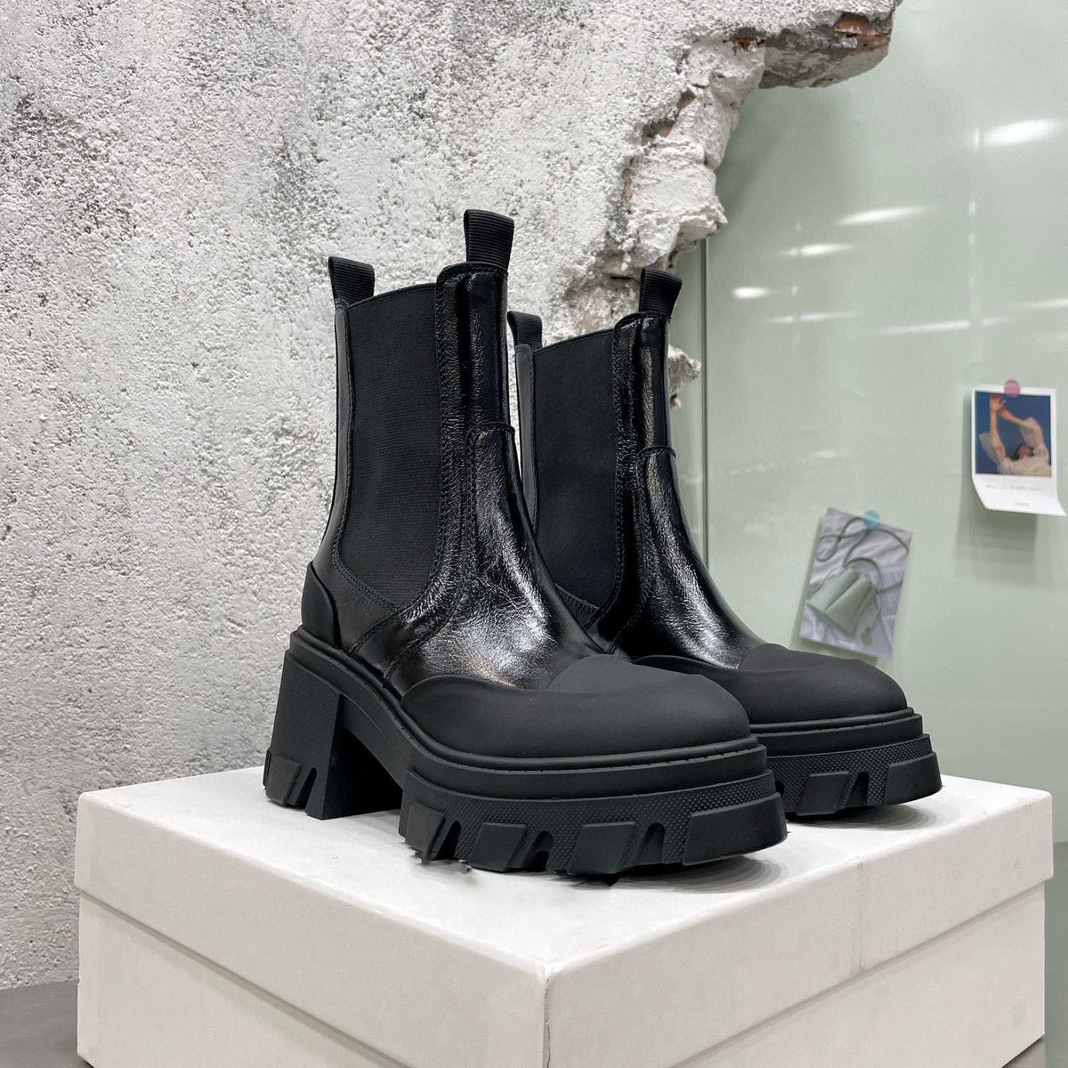 Black leather Chelsea boots with chunky lug soles and block heels, displayed on a white box.