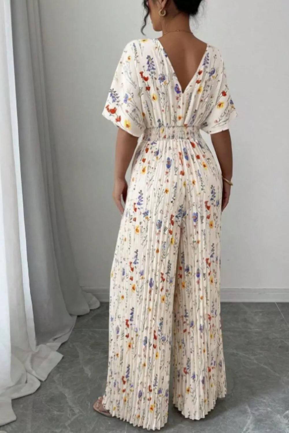 Floral print wide-leg pleated jumpsuit from Trendsi, featuring a stylish design with flowing fabric and vibrant flower patterns.