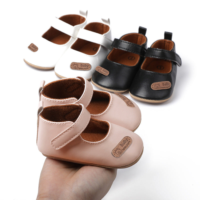 Pink, white, and black leather baby shoes with velcro straps, brown inner lining, and "Baby" brand labels on toes.