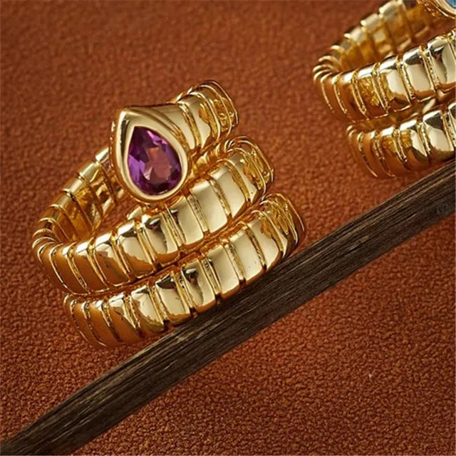 Gold snake-style metal ring with ribbed pattern and purple teardrop-shaped gemstone on the head.
