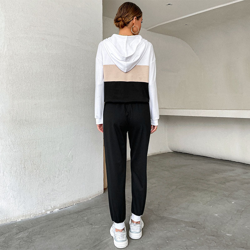 Rear view of a woman wearing a color-block hoodie and matching sweatpants in white, beige, and black.