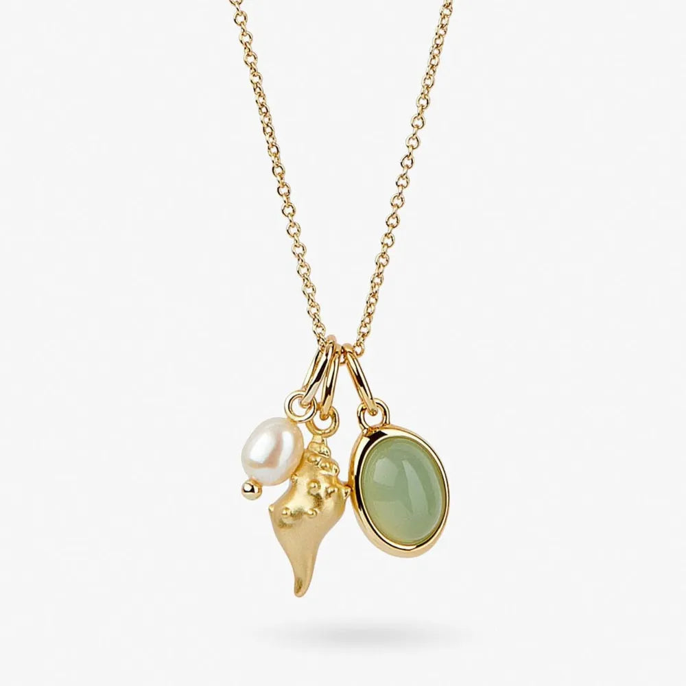 Gold charm necklace with a pearl, gold conch shell, and oval green gemstone pendant on a fine chain.