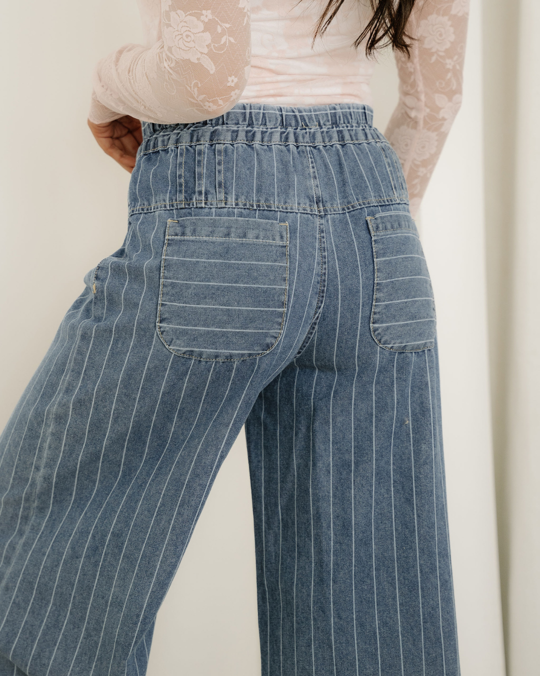 Back view of blue denim pinstripe wide-leg jeans featuring an elastic waist and two back pockets.