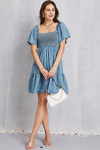 VYSN smocked square neck mini denim dress with sleeveless design and fitted waist, displayed on a hanger.