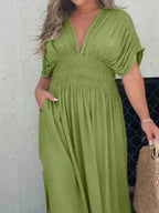 Plus size full-length maxi dress with slit, V-neck, and smocked waist by Trendsi, shown in a flowing fabric design.