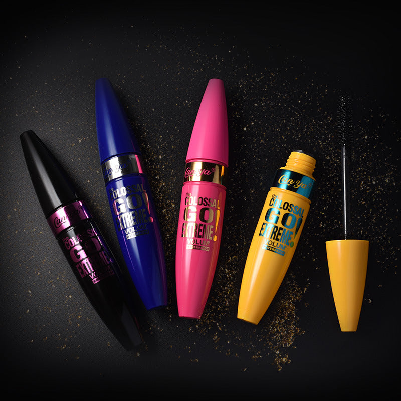 Four mascara tubes in black, blue, pink, and yellow, with one open showing its brush, on a black background.