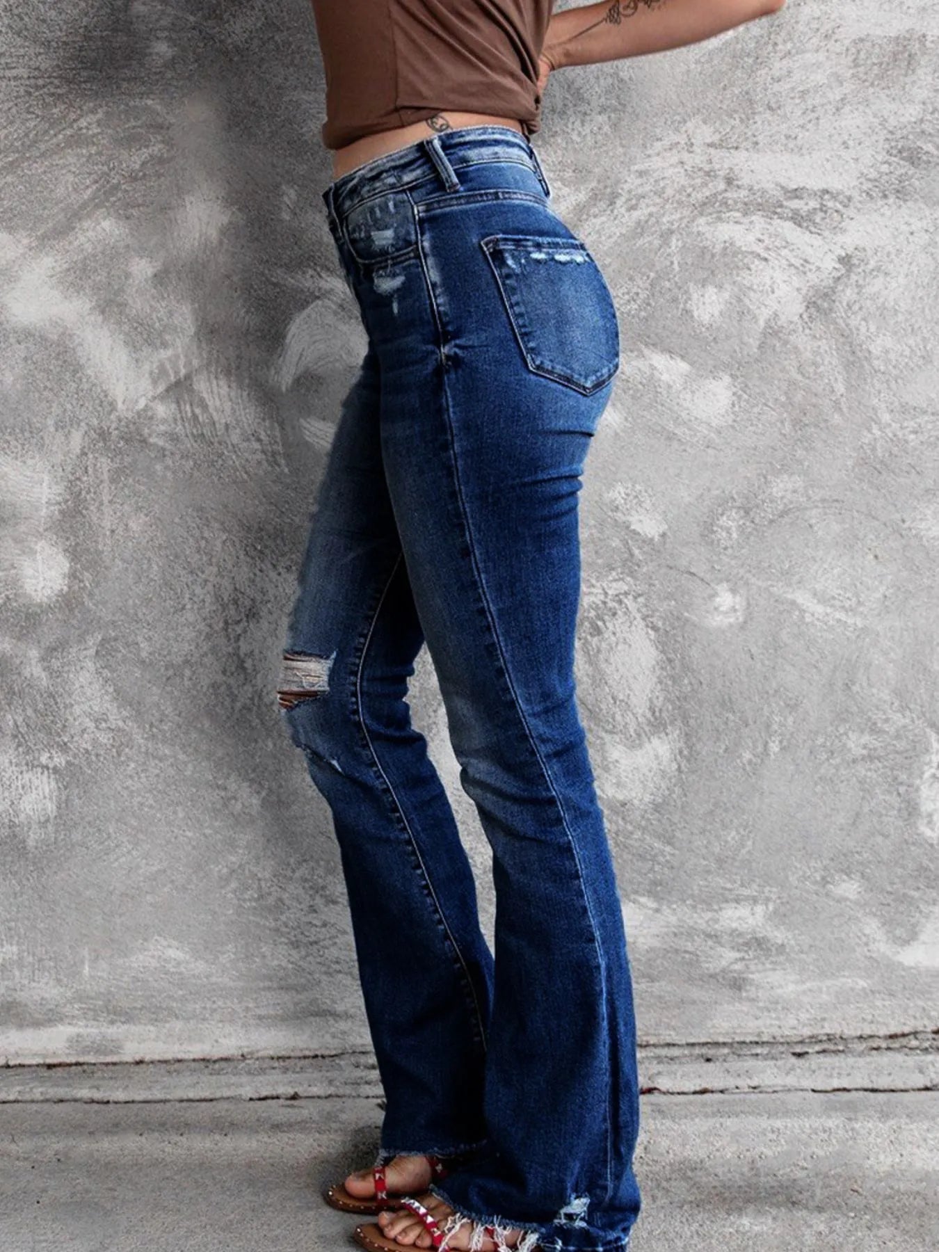 Distressed flare denim jeans by Plush Fashion Shop featuring ripped details and wide-leg fit on model.