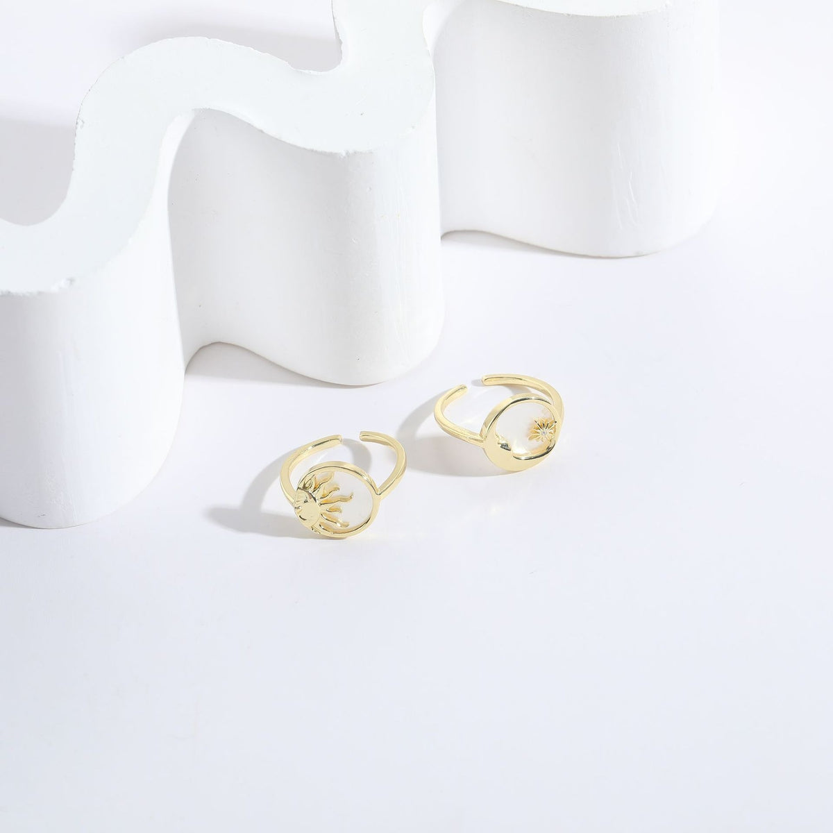 Two gold metal rings with open bands, featuring circular celestial designs of a sun and moon.