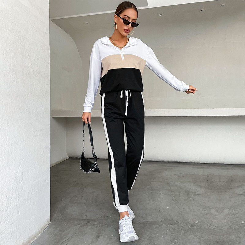 A model wears a white, tan, and black color-blocked tracksuit with a half-zip hoodie and drawstring jogger pants.
