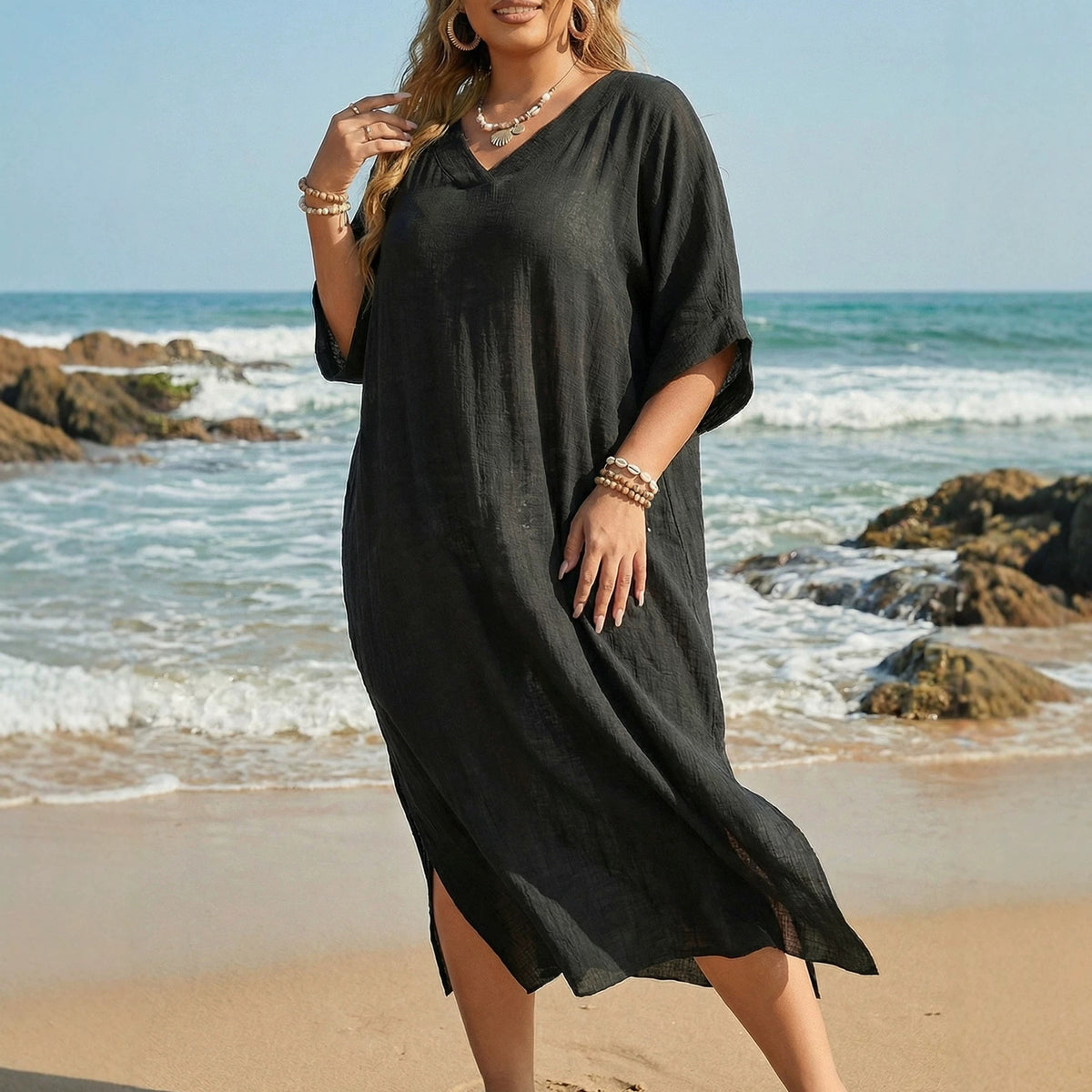 A plus-size woman in a solid black linen beach cover-up with a V-neck, short sleeves, and side slits on a beach.