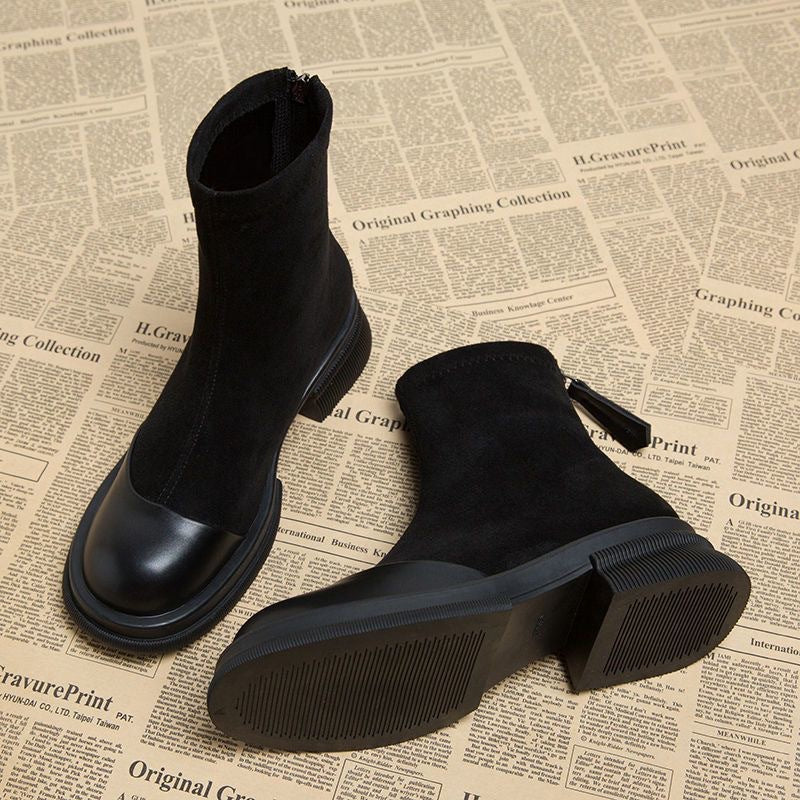 Black suede ankle boots with round toe, chunky rubber sole, and back zipper on a newspaper background.