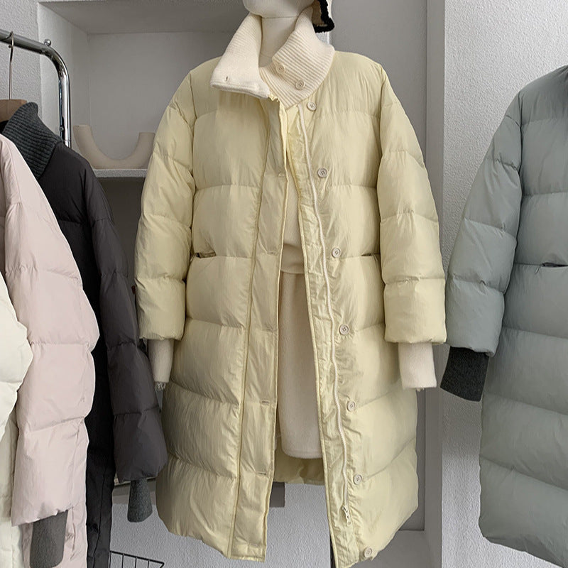A pale yellow long puffer coat with a knit stand-up collar is displayed on a mannequin.