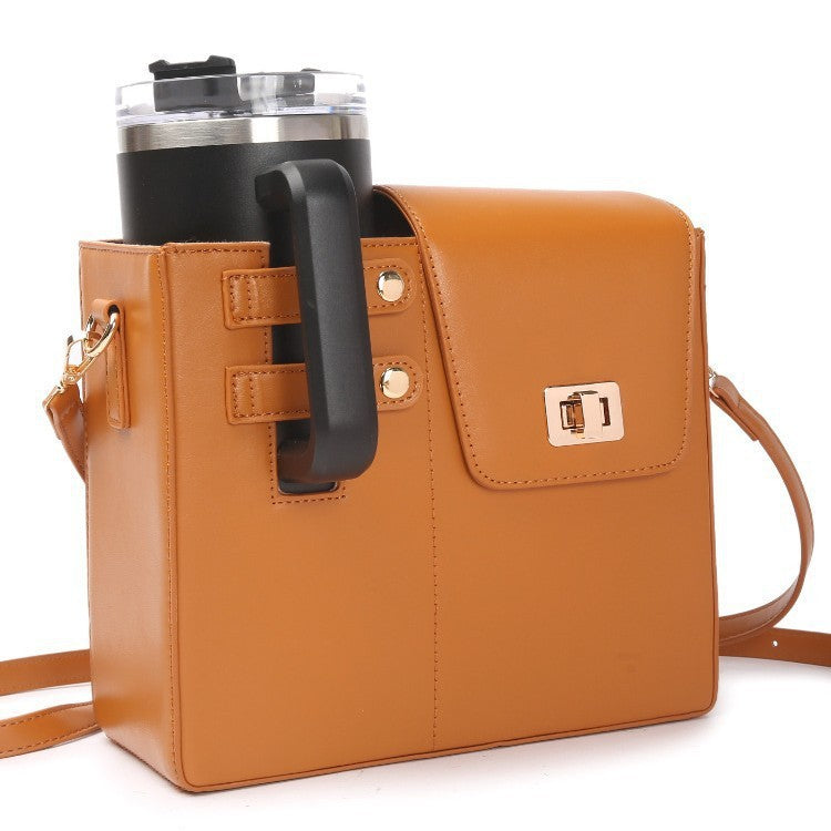 Tan leather crossbody bag holding a black tumbler with a handle, featuring a flap closure and gold-tone hardware.