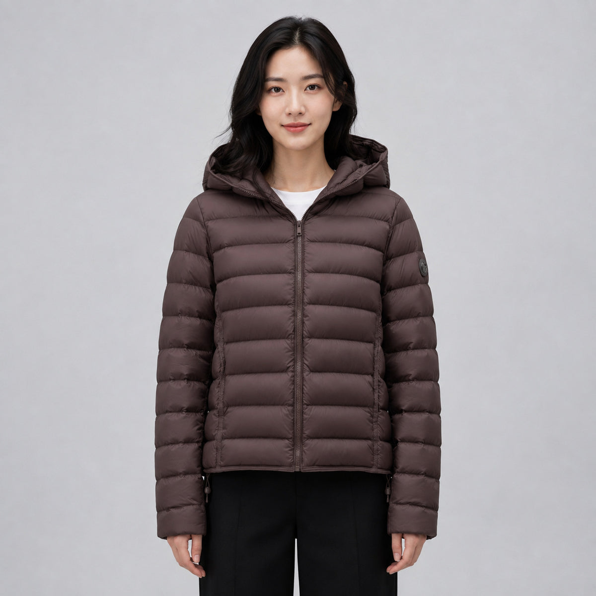 Brown hooded puffer jacket in quilted nylon with a front zipper, worn by a model.