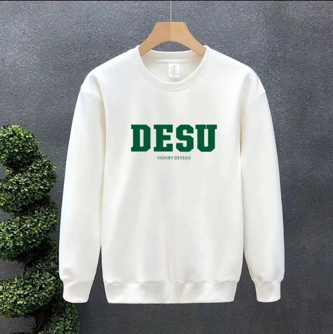 White crewneck sweatshirt with green "DESU" varsity lettering on the chest, hanging on a hanger.