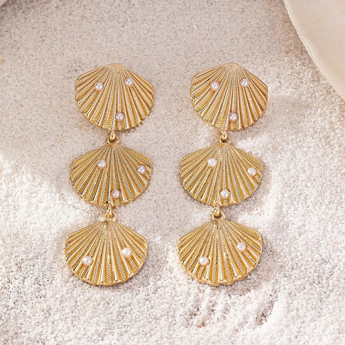 Seashell dangle earrings with pearl accents, featuring gold hooks and intricate shell designs for a stylish beach-inspired look.