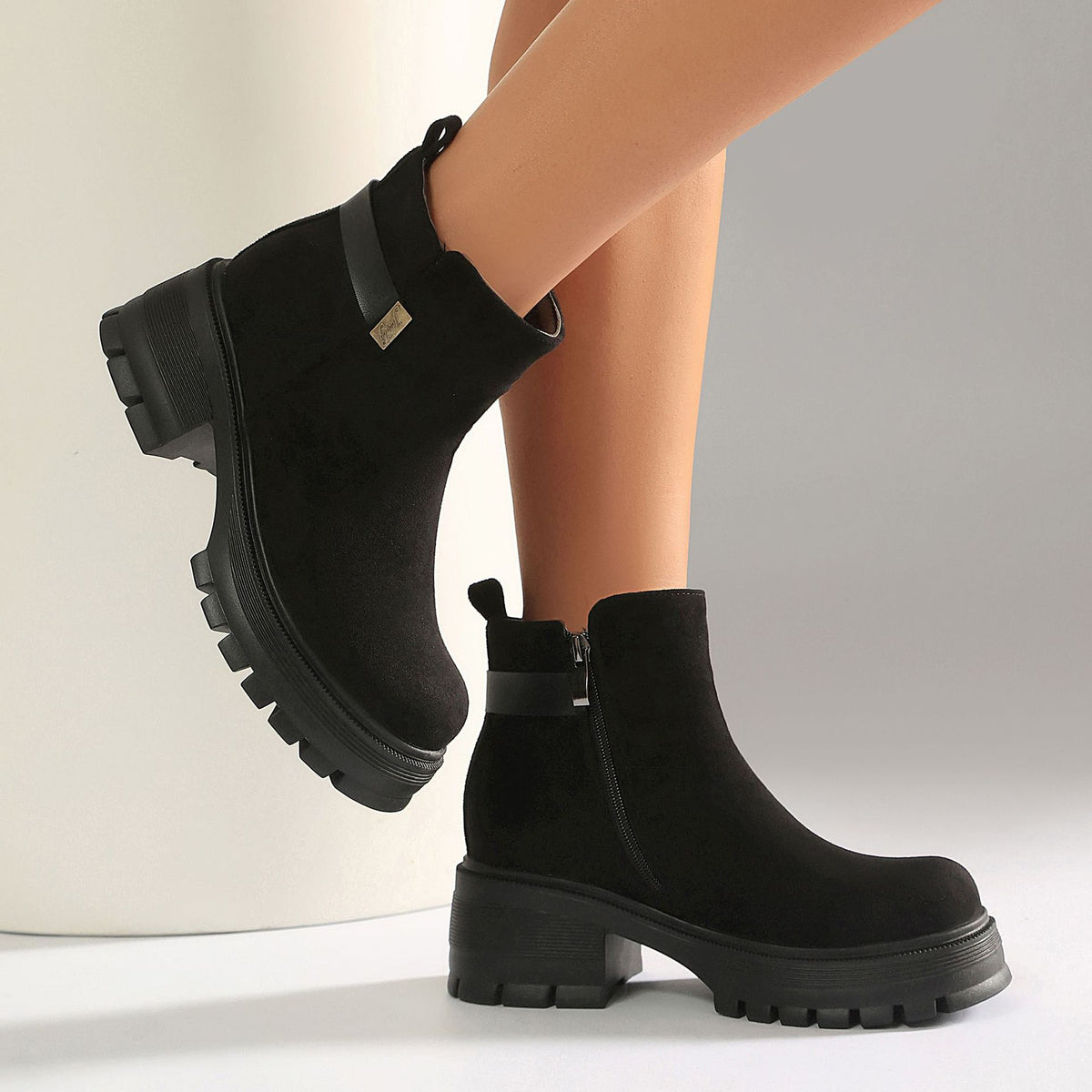 Black suede ankle boots with chunky lug soles, a side zipper, and a small strap with a metallic buckle detail.