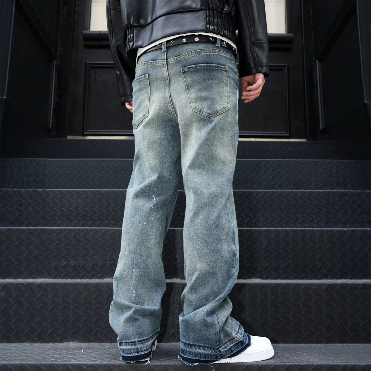 Back view of blue denim jeans with a distressed, paint-splatter pattern, relaxed style, and frayed cuffs.