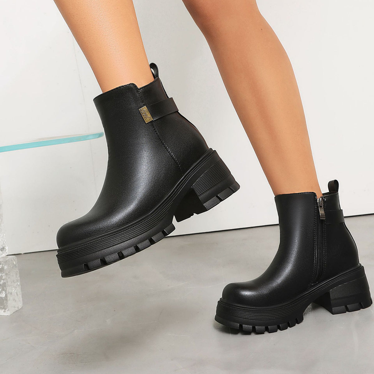 Black faux leather ankle boots with thick lug soles, block heels, side zippers, and buckled straps.