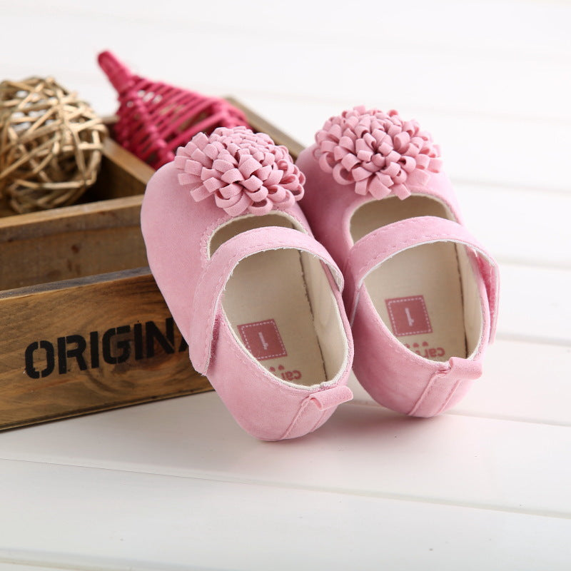 Pink faux suede baby shoes with a strap and large ruffled flower on each toe.