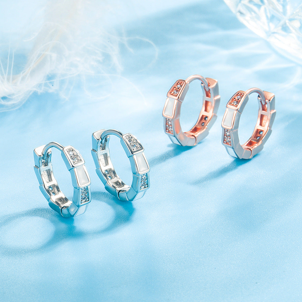 Two pairs of geometric metal hoop earrings, one silver and one rose gold, set with white enamel and clear stones.