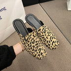 Pointed-toe mule slippers featuring a tan and black leopard print fabric upper with black insoles.