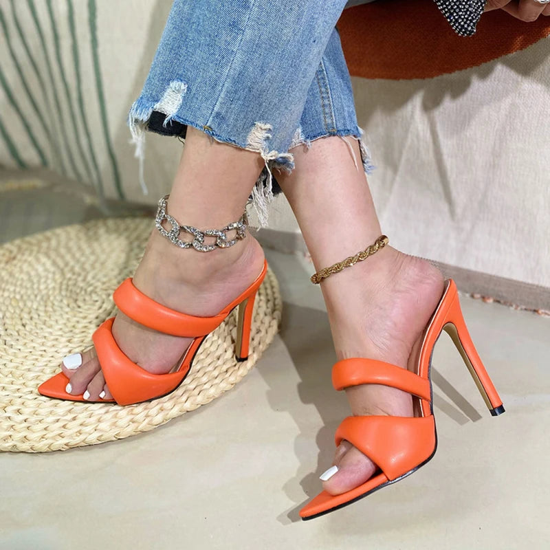 Orange faux leather pointed-toe mules with two padded straps and high stiletto heels, worn with anklets and jeans.