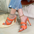 Orange faux leather pointed-toe mules with two padded straps and high stiletto heels, worn with anklets and jeans.