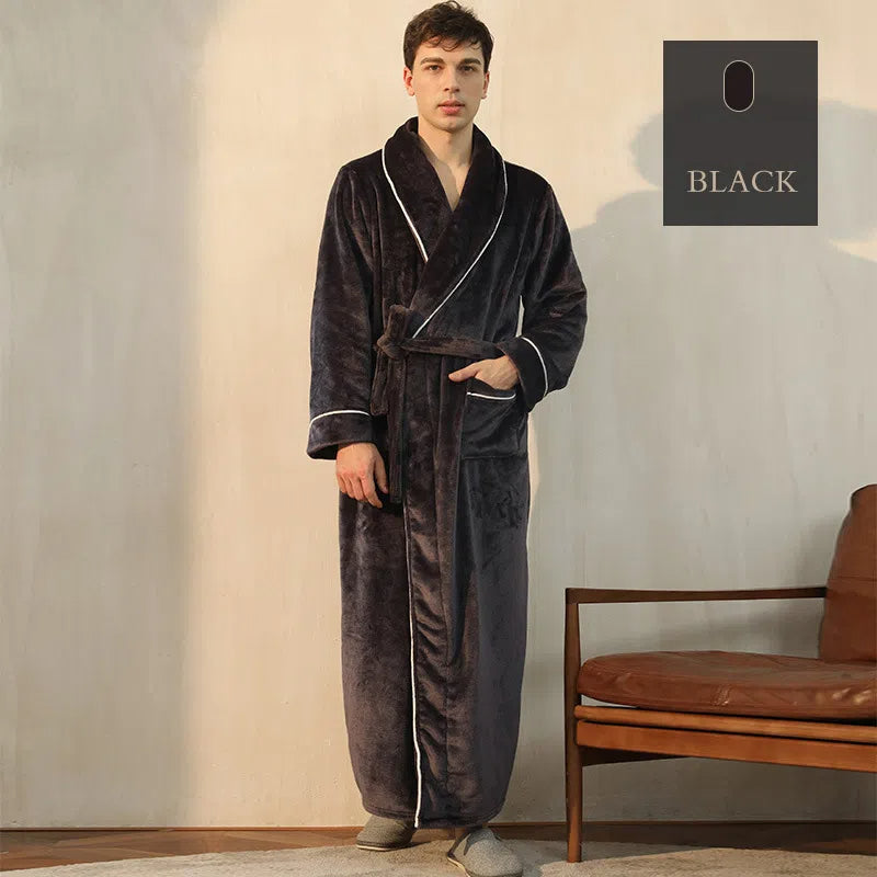 A man wears a black fleece bathrobe with white piping and waist tie, standing in a room.